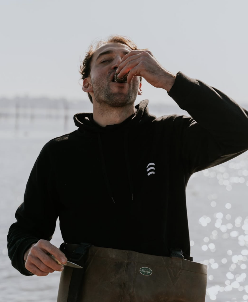 un homme (le créateur) qui mange une huitre devant la mer 