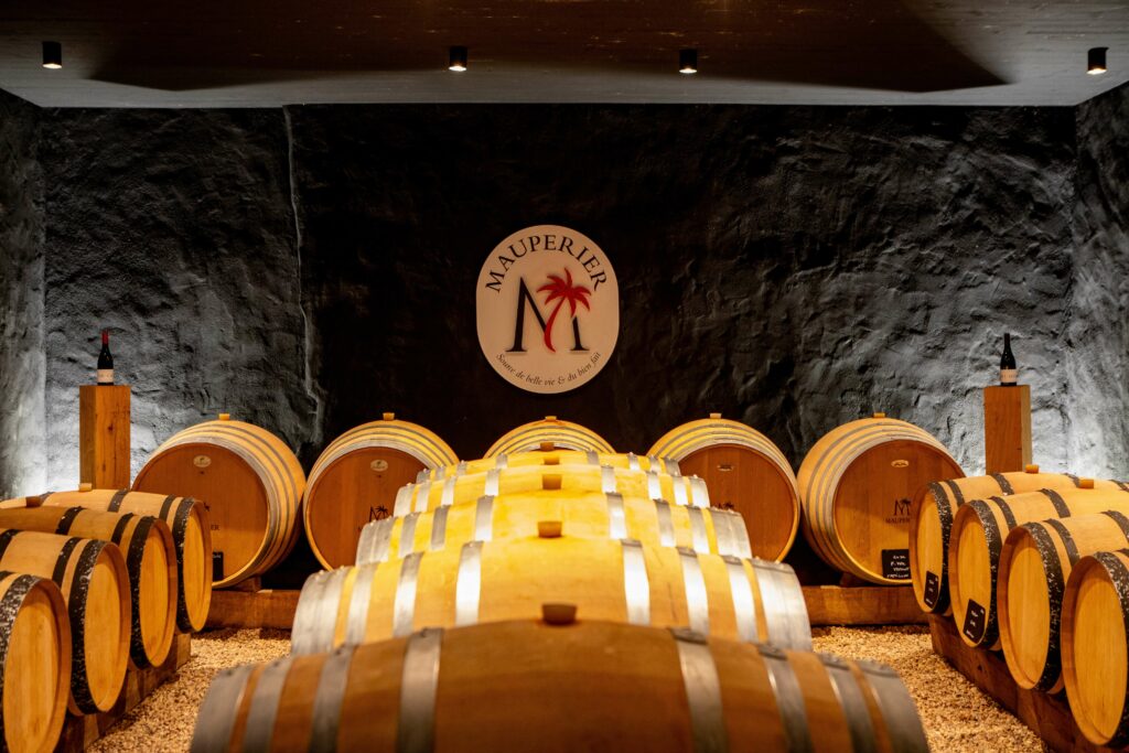 Le cellier du Château de Mauperier en appellation Gaillac. On voit leurs barriques de chênes posées sur des racs au sol, ainsi que leur logo sur le mur du fond